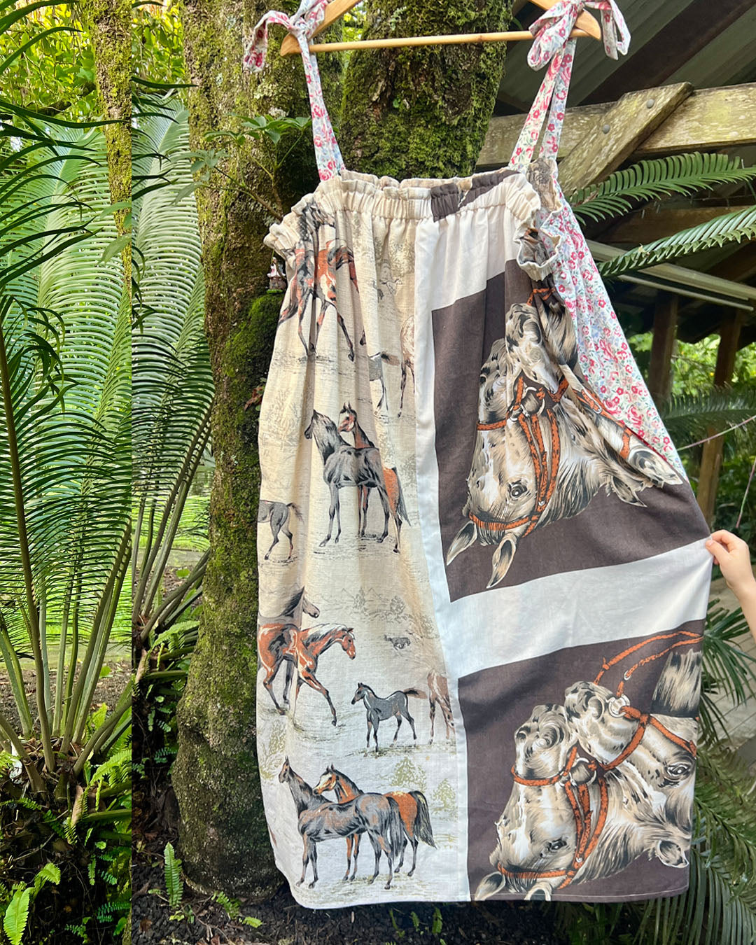 Lucky horse plus size, one size, easywear, oversize tea party dress with adjustable straps, elasticised neckline and upcycled, recycled, vintage, heirloom, patchwork fabrics. Vintage fabrics depict lucky horses for the Chinese Lunar New Year of the horse. Lucky Horse dress is hanging on a beautiful tree in a lush garden