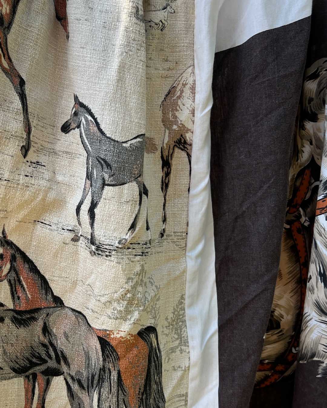 A close-up of a fabric product featuring a rustic print of horses and donkeys in earthy tones, with a prominent dark brown vertical panel and a white border.