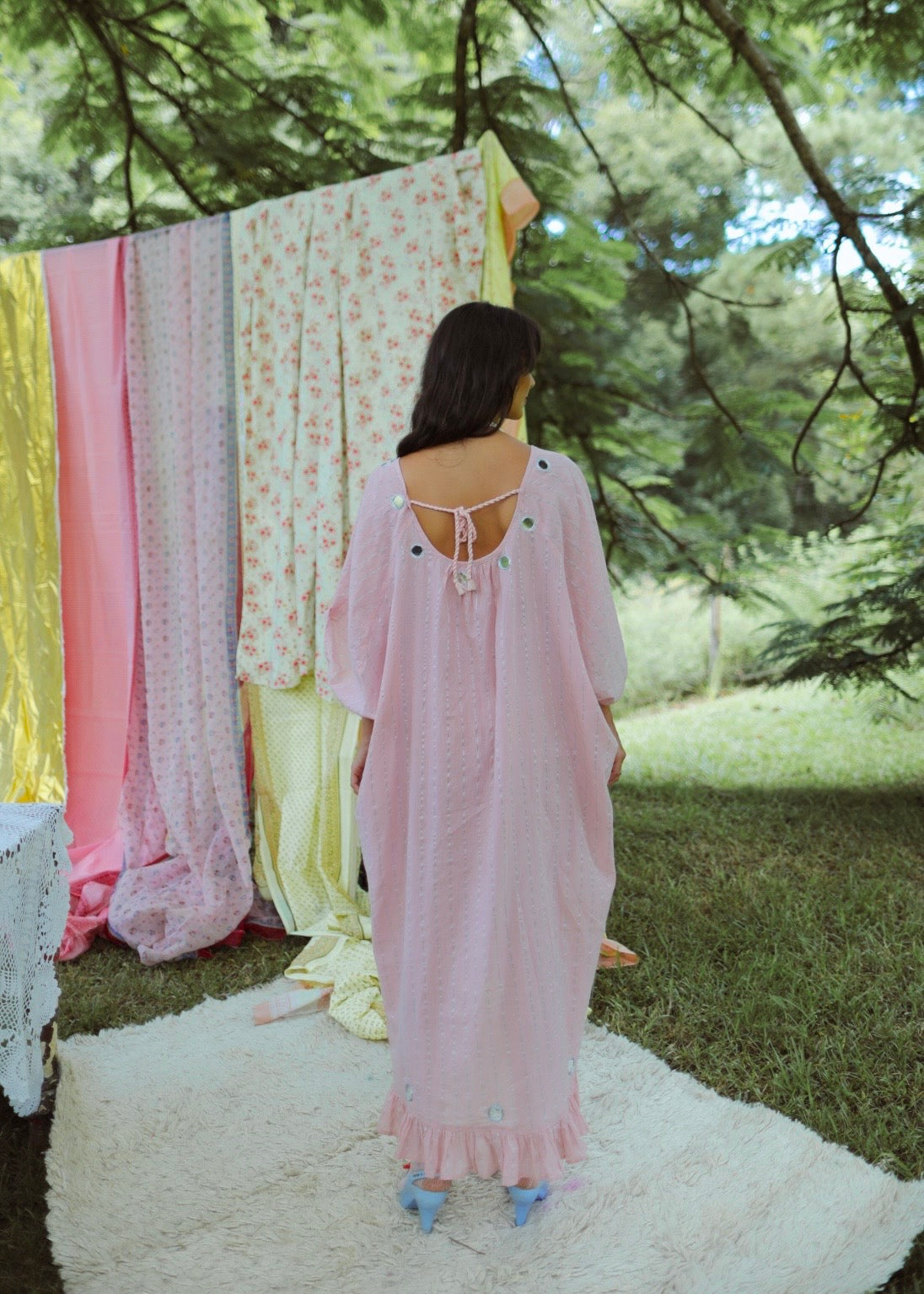 Dark haired woman in a one size, plus size, free size, pink dress with silver lurex strip and indian mirrorwork in an outdoor garden setting