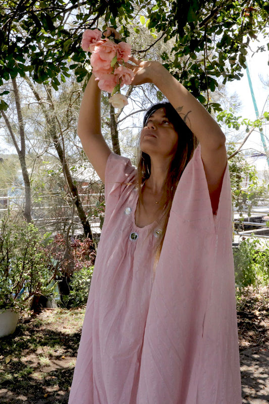 Woman in a one size, plus size, free size, pink dress with silver lurex strip and indian mirrorwork holding flowers in an outdoor , seaside setting