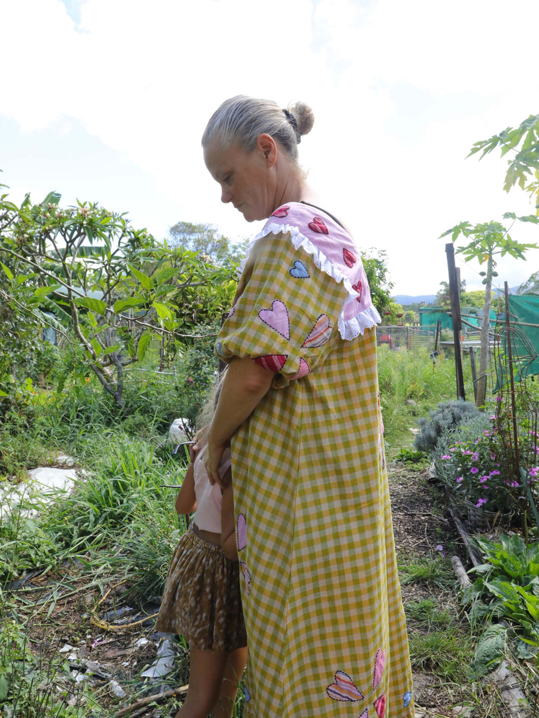 Woman in a yellow checkered dress with floral patterns in a garden setting