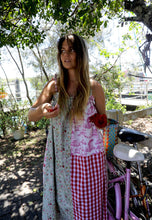 Load image into Gallery viewer, Woman in a floral dress with a checkered skirt standing outdoors near a bicycle.