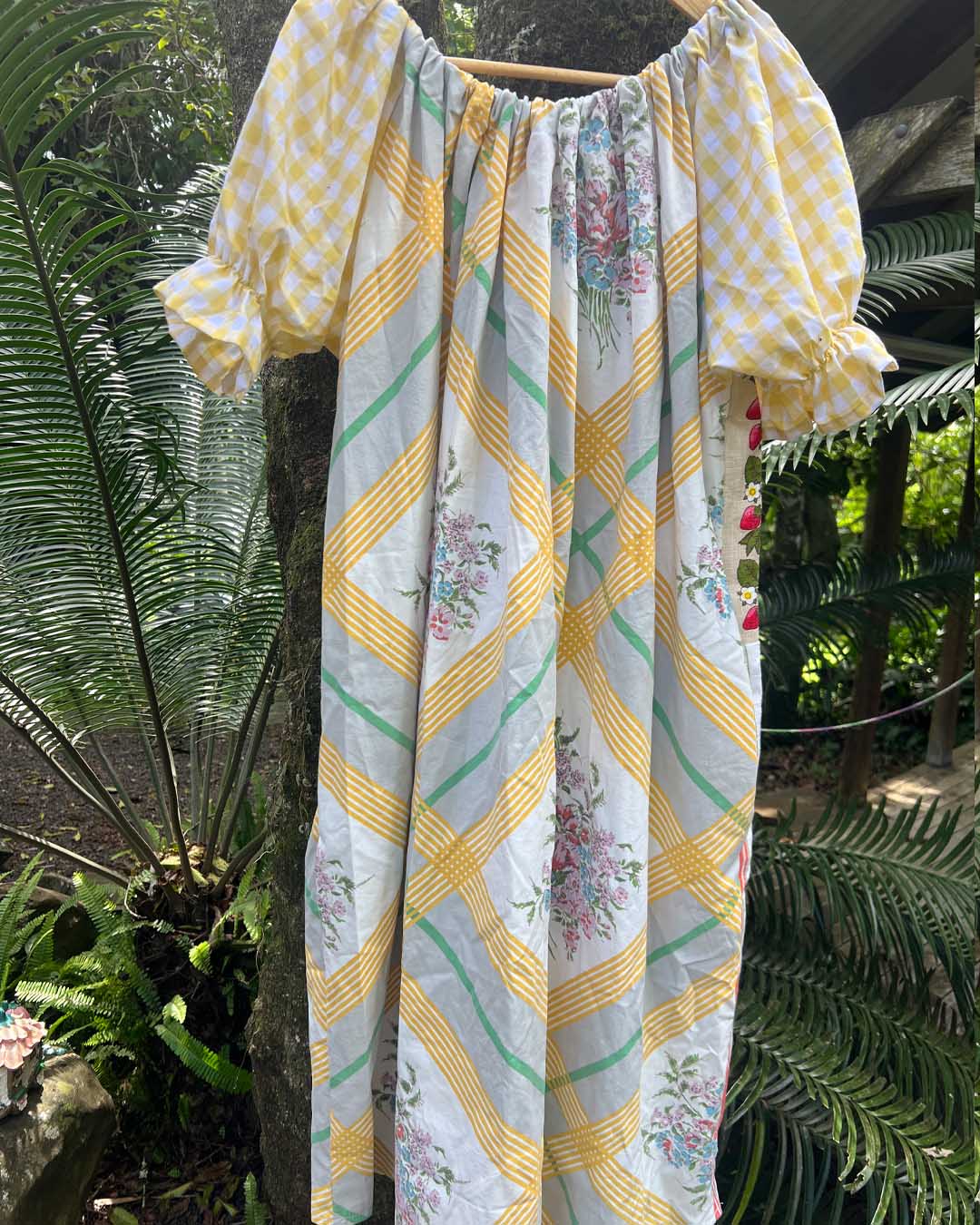 Floral and checkered dress hanging against a green leafy background