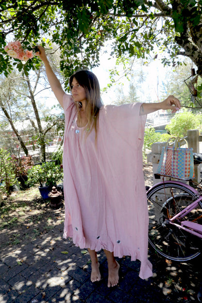 Woman in a one size, plus size, free size, pink dress with silver lurex strip and indian mirrorwork holding flowers in an outdoor , seaside setting