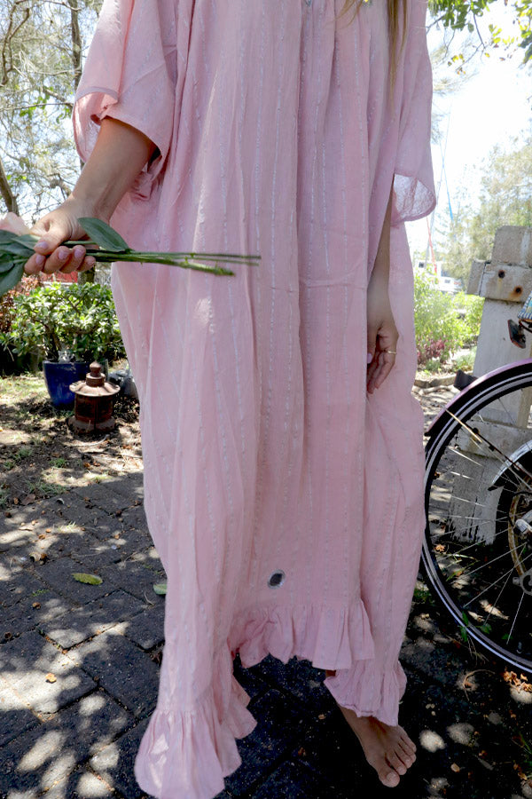 Woman in a one size, plus size, free size, pink dress with silver lurex strip and indian mirrorwork holding flowers in an outdoor , seaside setting