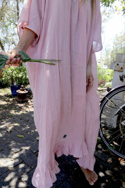 Woman in a one size, plus size, free size, pink dress with silver lurex strip and indian mirrorwork holding flowers in an outdoor , seaside setting