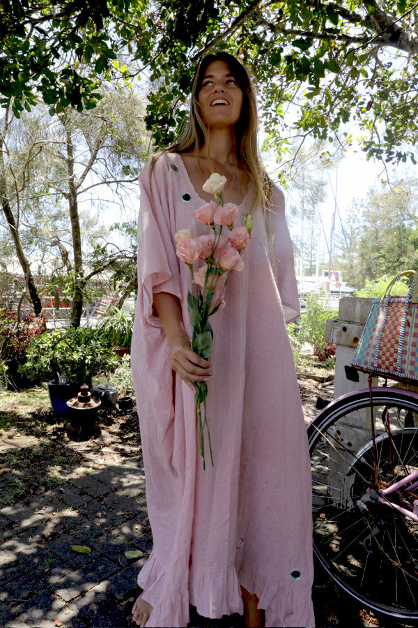 Woman in a one size, plus size, free size, pink dress with silver lurex strip and indian mirrorwork holding flowers in an outdoor , seaside setting