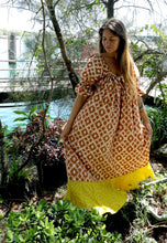 Load image into Gallery viewer, Indian batik cotton smock dress with puff sleeves and neon yellow bandhani tie dye frill worn by a woman standing in a waterfront garden