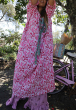 Load image into Gallery viewer, Woman in a pink floral dress standing next to a purple bicycle in a garden setting.