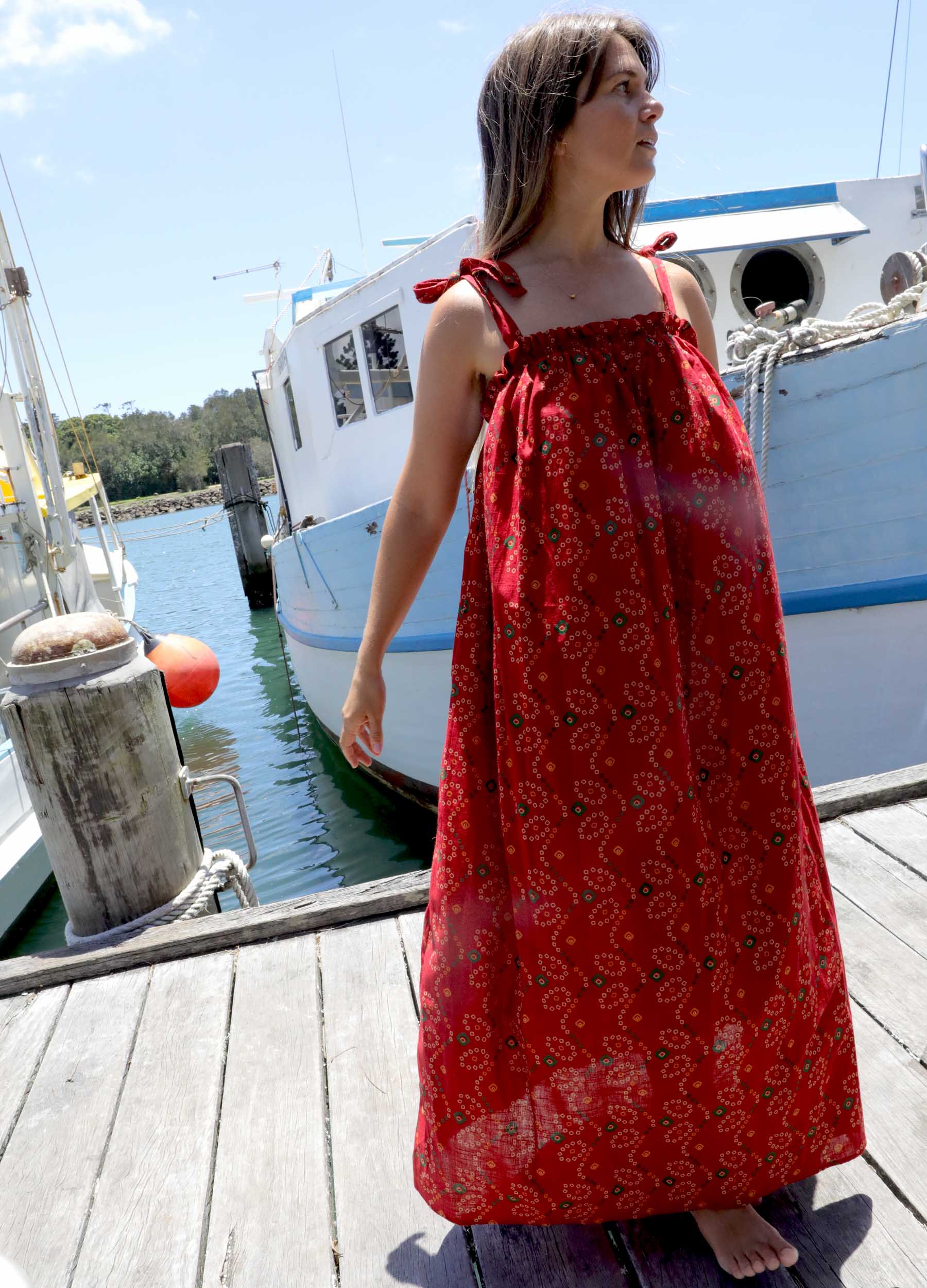 Woman in a plus size, one size, bohemian red dress standing on a dock with boats in the background
