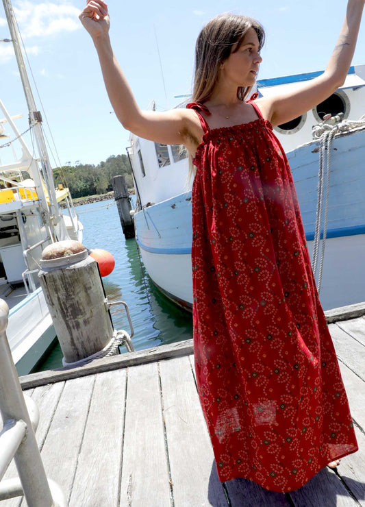 Woman in a plus size, one size, bohemian red dress standing on a dock with boats in the background