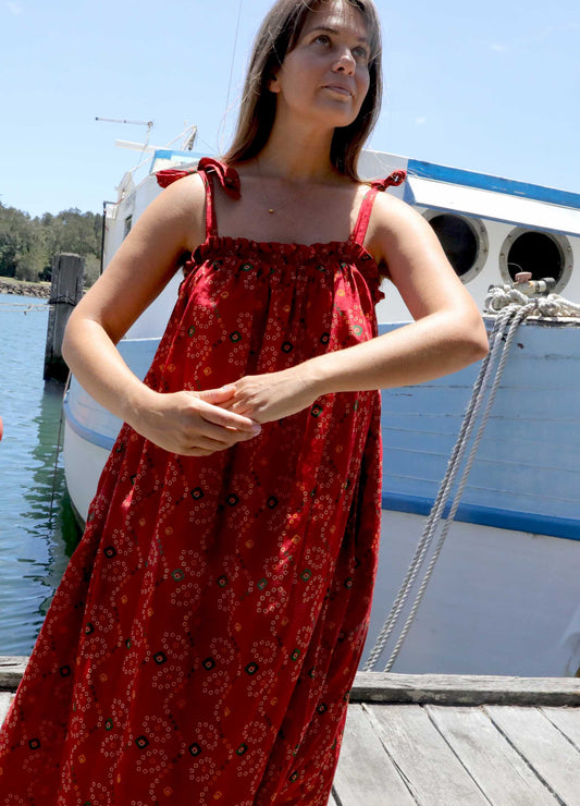 Woman in a plus size, one size, bohemian red dress standing on a dock with boats in the background