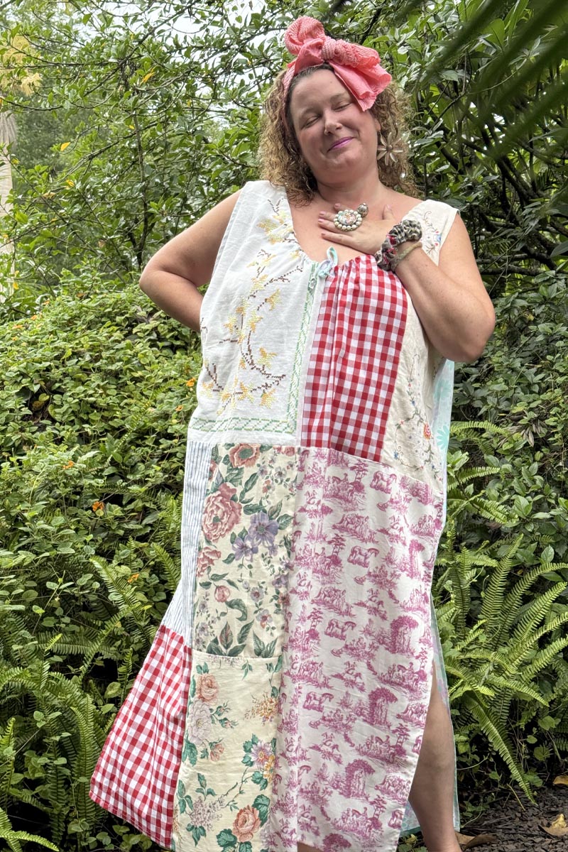 Woman wearing a patchwork dress with floral, checkered, and abstract patterns in a garden setting.