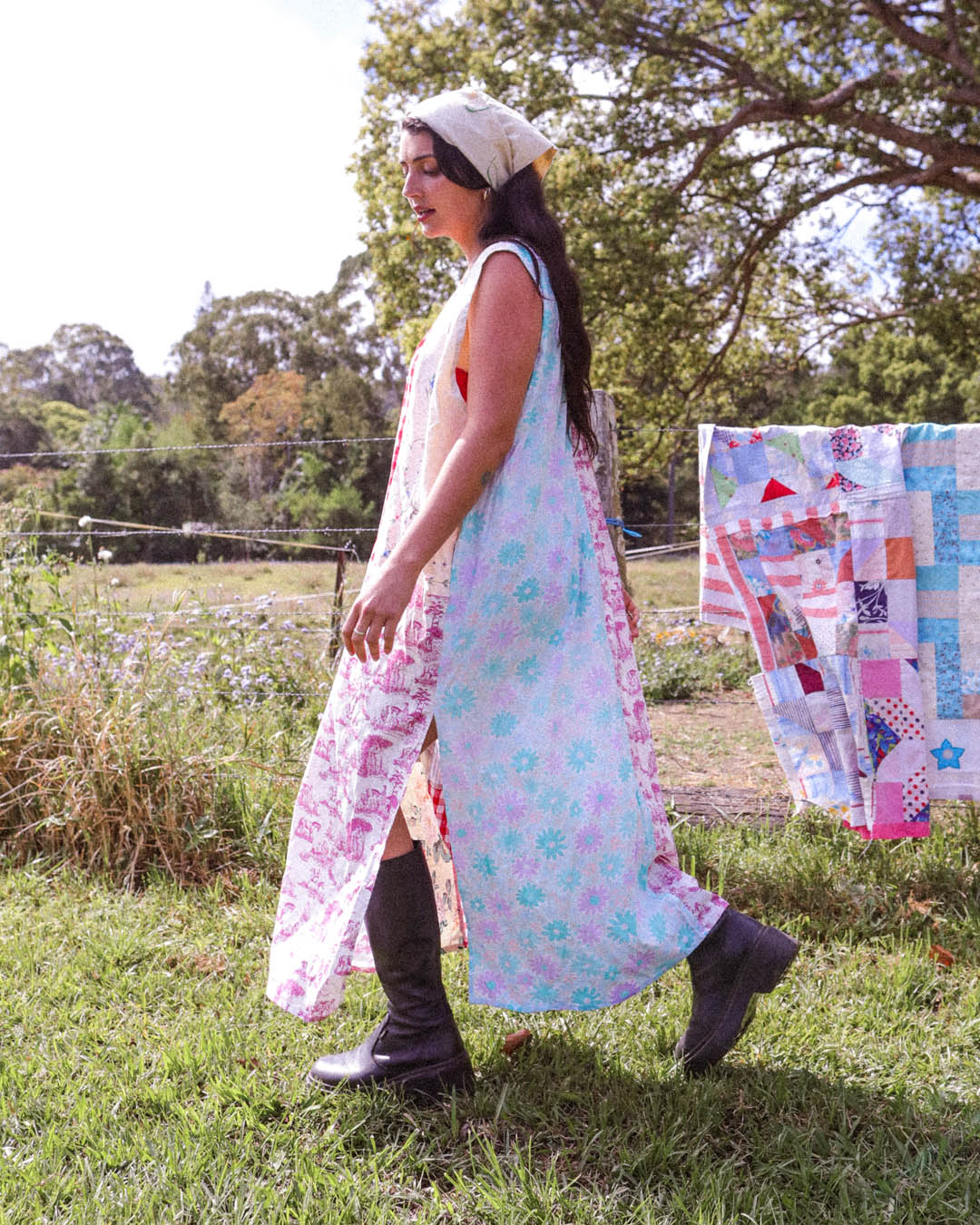 A woman wearing a long sleeveless floral dress walks outdoors on a grassy lawn. The dress has a light blue, pink, and purple floral pattern.