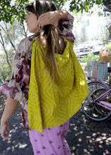 Load image into Gallery viewer, Woman wearing a pink and chartreuse handblock patterned top with holy cow motif and purple pants standing outdoors with trees and plants in the background. A perfect Christmas Fashion Outfit and Black Friday Sale