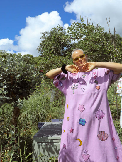Person wearing a purple dress with colorful applique in an outdoor setting