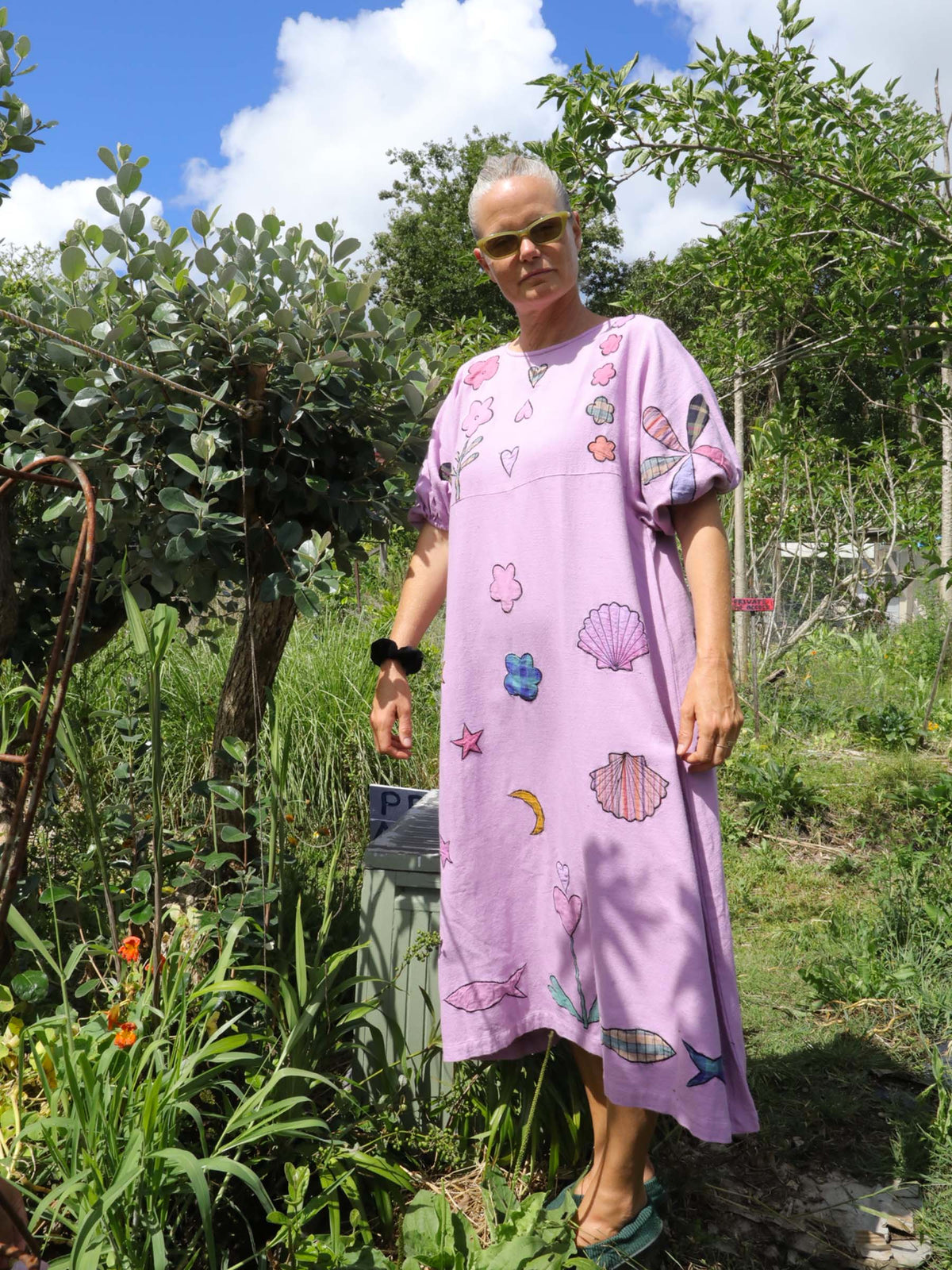 Person wearing a pink dress with shell patterns in a garden setting