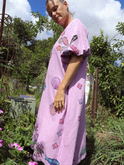 Person wearing a pink dress with floral and shell applique patterns in an outdoor setting