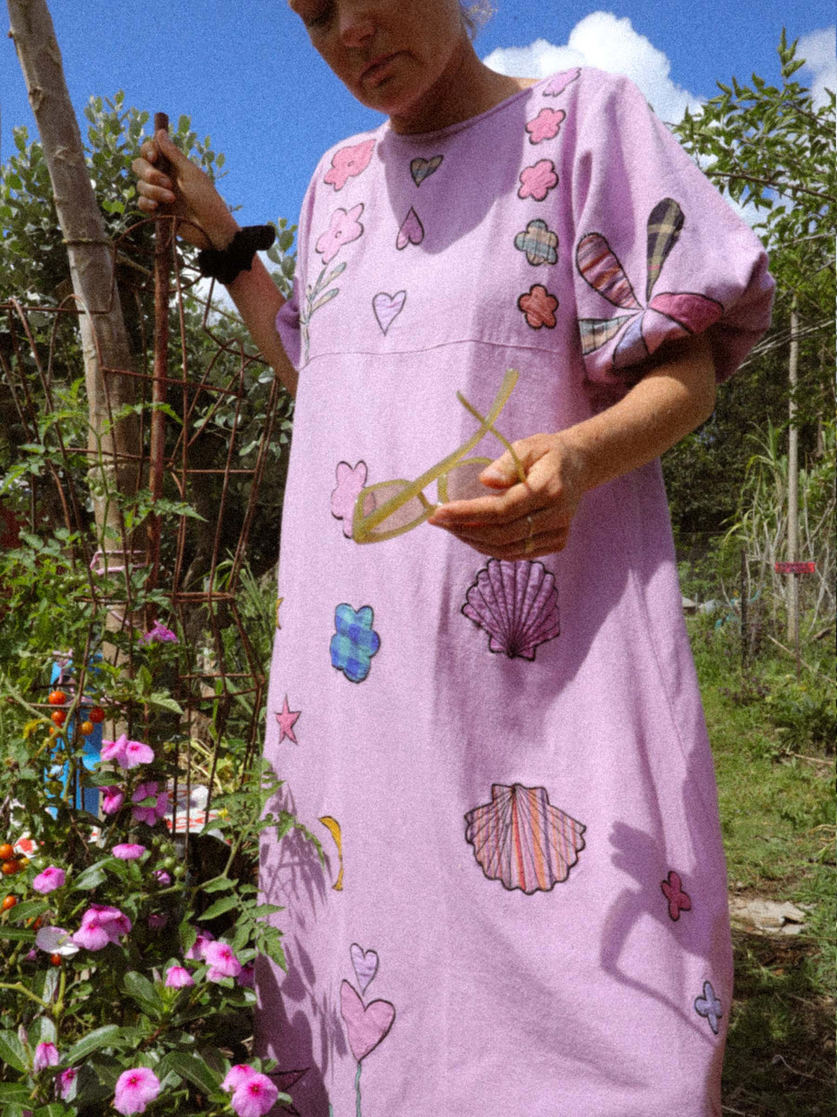 Person wearing a pink dress with floral and fish and shell applique patterns in a garden setting