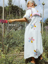 Load image into Gallery viewer, Person wearing a white dress with colorful floral applique patterns in an outdoor setting.