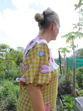 Load image into Gallery viewer, Person wearing a yellow checkered dress with pink hearts in a garden setting