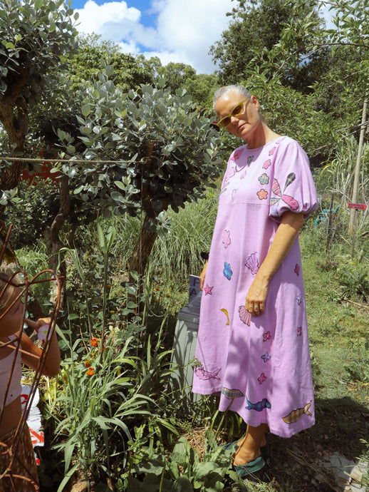 Woman in a pink embroidered dress standing in a garden with trees and plants around.