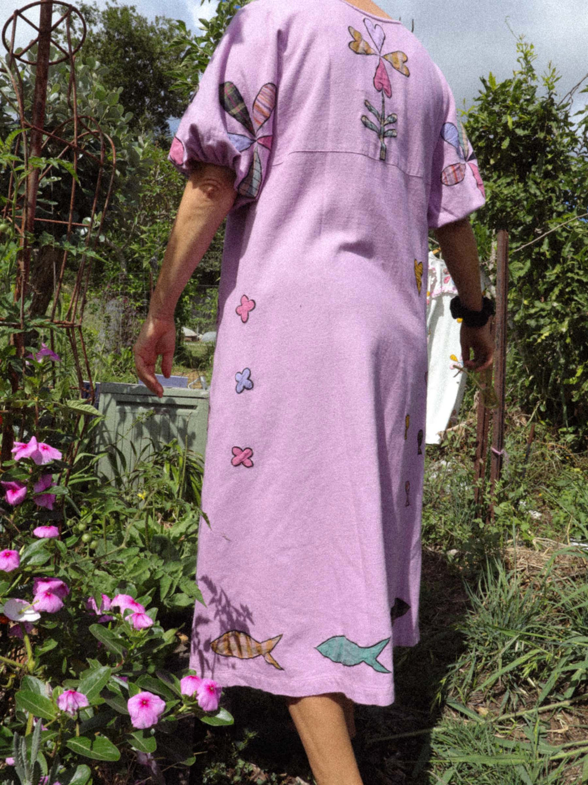 Person wearing a pink dress with flowers and fish applique in a garden setting