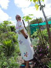 Load image into Gallery viewer, Person wearing a white dress with colorful floral applique patterns in a garden setting