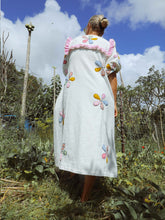 Load image into Gallery viewer, Person wearing a white dress with colorful floral embroidery in an outdoor setting.