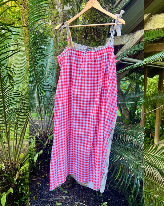 Red and white checkered dress on a hanger with green foliage in the background