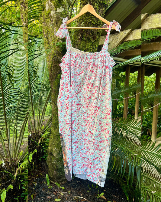 Floral dress hanging on a wooden hanger against a lush green forest background