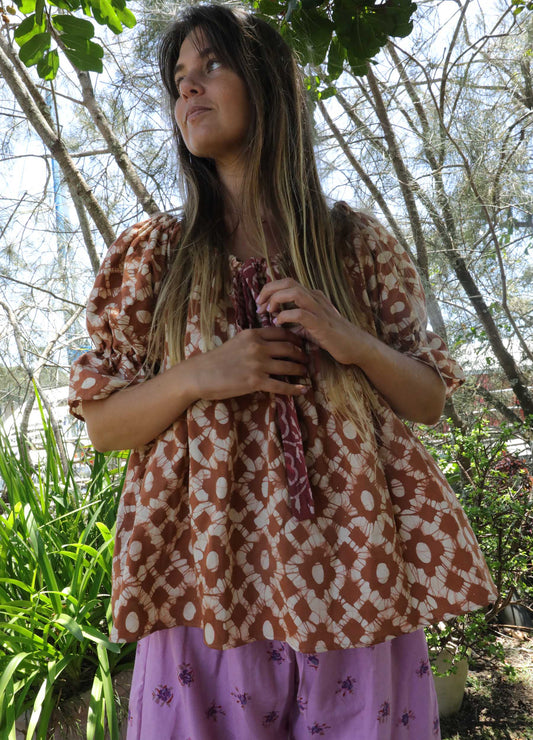 Woman wearing an ochre handblock patterned top and purple skirt standing outdoors with trees and plants in the background. A perfect Christmas Fashion Outfit and Black Friday Sale