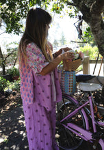 Load image into Gallery viewer, Woman in a pink floral dress standing next to a purple bicycle in an outdoor setting.