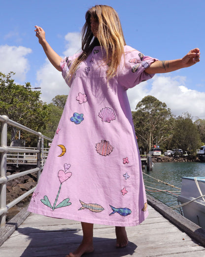 Person wearing an orchid pink dress with colorful applique embroidery standing on a dock by a body of water. One size, plus size, bohemia, Christmas fashion, Christmas Dress