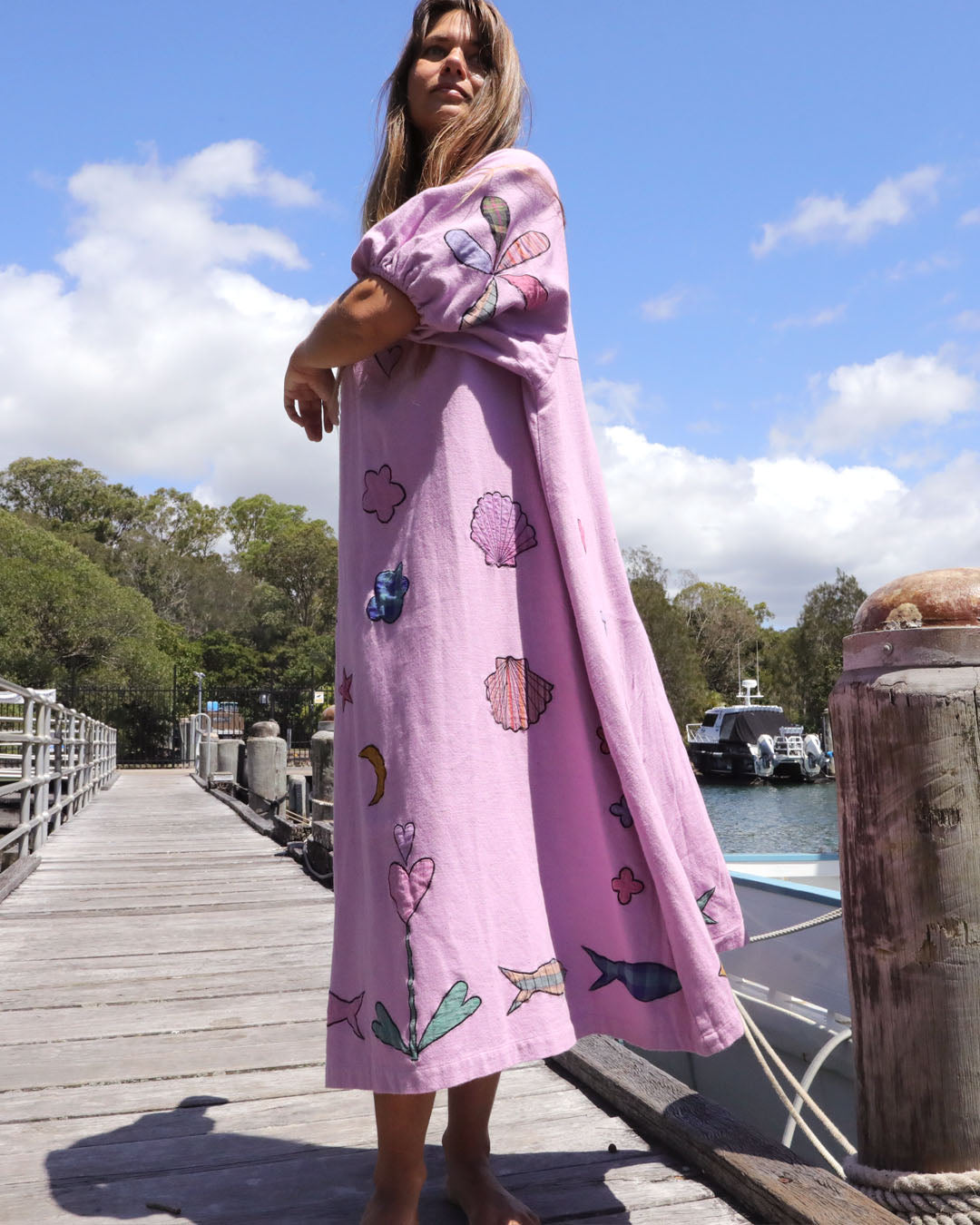 Person wearing an orchid pink dress with colorful applique embroidery standing on a dock by a body of water. One size, plus size, bohemia, Christmas fashion, Christmas Dress