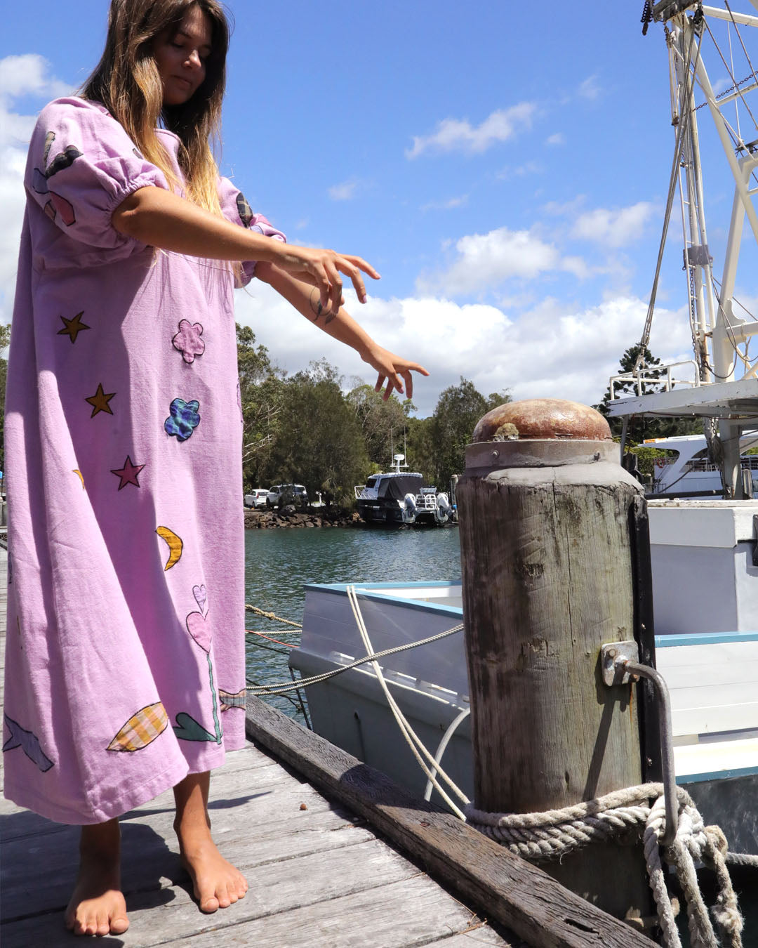 Person wearing an orchid pink dress with colorful applique embroidery standing on a dock by a body of water. One size, plus size, bohemia, Christmas fashion, Christmas Dress