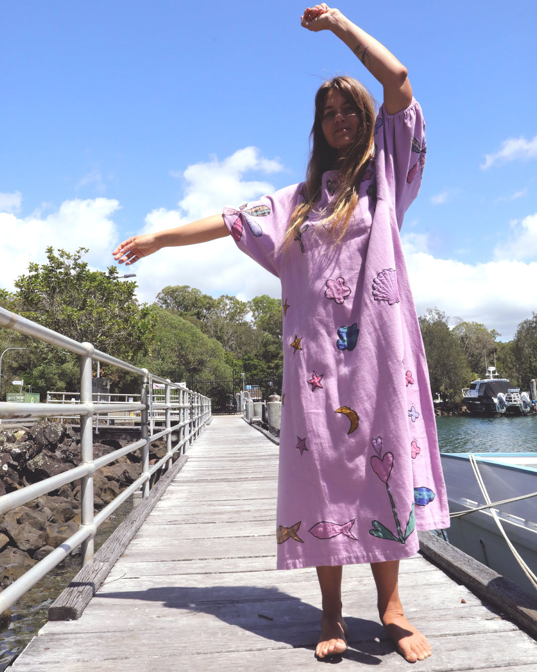 Person wearing an orchid pink dress with colorful applique embroidery standing on a dock by a body of water. One size, plus size, bohemia, Christmas fashion, Christmas Dress