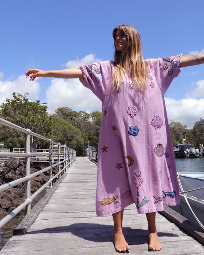 Person wearing an orchid pink dress with colorful applique embroidery standing on a dock by a body of water. One size, plus size, bohemia, Christmas fashion, Christmas Dress