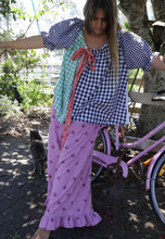 Load image into Gallery viewer, Woman in a checkered top and pink skirt standing next to a pink bicycle with a cat nearby.