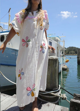 Person wearing a one size, plus size, bohemian white dress with colourful flower applique standing on a boat docked at a pier. Great Christmas Dress and black friday sale